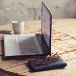 Wooden table with laptop, glasses, wallet and cup of coffee